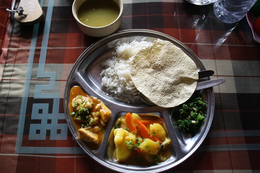 A steel plate of dal bhat with rice, papad, vegetable curries and greens on a teahouse table in Namche Bazaar