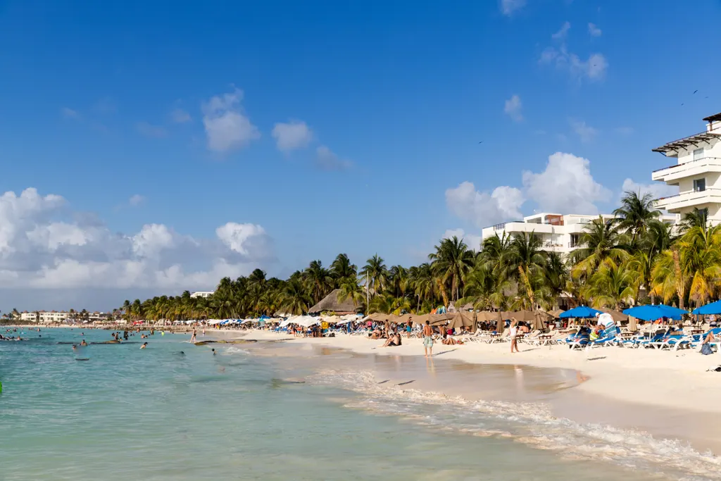 Shallow turquoise water and white sand lined with palm trees and parasols at Playa Norte on Isla Mujeres